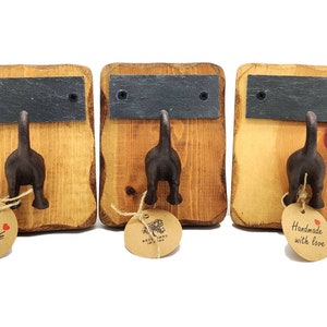 Może przedstawiać: Trzy drewniane wieszaki ścienne z wzorem czarnego psiego ogona. Każdy wieszak ma małą czarną tabliczkę z łupka i brązową papierową etykietę z napisem "Ręcznie robione z miłością".