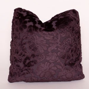 Peut inclure: Un oreiller en peluche avec un tissu en velours violet foncé et un motif damassé.