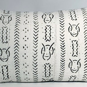 Puede incluir: Almohada blanca con patrones geométricos negros, incluyendo chevron y figuras estilizadas. La almohada está hecha de una tela tejida con una superficie ligeramente texturizada.