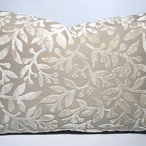 Puede incluir: Una almohada beige con un patrón floral blanco. La almohada está hecha de una tela suave y aterciopelada.