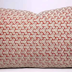 Puede incluir: Una almohada de color rojo y blanco con un diseño geométrico. La almohada está hecha de una tela suave y texturizada.