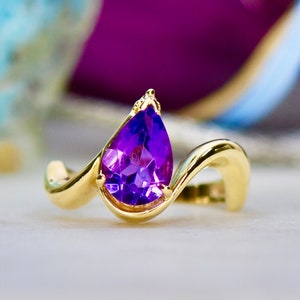 May include: A gold ring with a pear-shaped amethyst gemstone. The ring has a curved band.