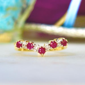 May include: A gold band ring with a V-shaped row of red rubies and white diamonds.