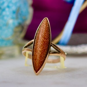May include: A gold ring with a brown, oval-shaped gemstone. The gemstone has a sparkly, textured surface.