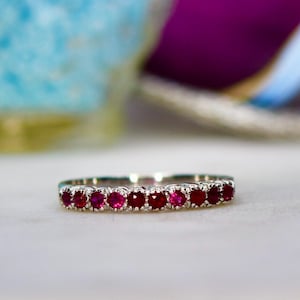 May include: A delicate silver band ring with a row of small, round, red ruby gemstones.