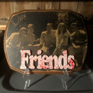 May include: A wooden plaque with a photo of four friends and the word "Friends" in white letters with red splatters.