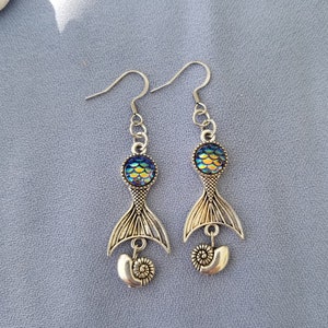 May include: A pair of silver mermaid tail earrings with iridescent blue and green scales and a seashell charm.
