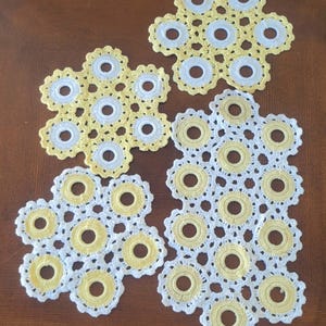 Puede incluir: Cuatro posavasos hechos a mano de ganchillo con un diseño floral. Los posavasos son blancos y amarillos, con un patrón circular en el centro de cada flor. El trabajo de ganchillo es detallado e intrincado.