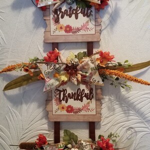 以下が含まれることがあります： 秋をテーマにした装飾が施された木製の看板が3つあり、それぞれに異なる言葉が書かれています。「感謝」「感謝」「祝福」です。看板は秋の葉、花、貝殻で飾られています。