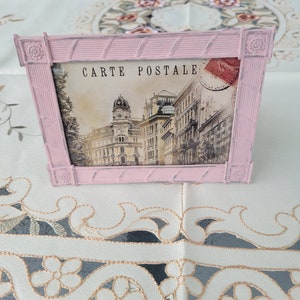 Puede incluir: Un marco de fotos rosa con una postal vintage en su interior. La postal presenta una foto en blanco y negro de un edificio con el texto "CARTE POSTALE" impreso en la parte superior.