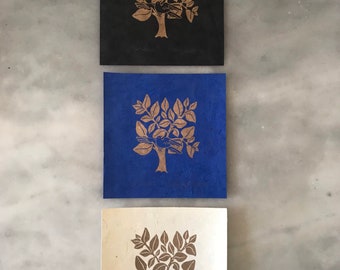 May include: Three prints of a gold tree with a bird on a branch. The prints are on black, blue, and white paper.