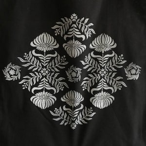 May include: A black fabric with a white floral design. The design is symmetrical and features a repeating pattern of flowers and leaves.