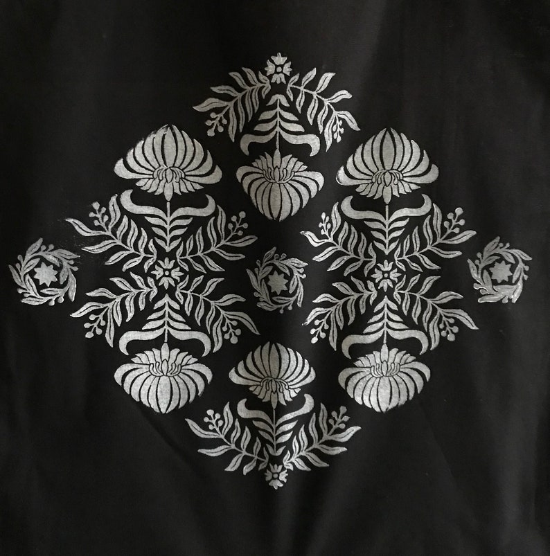 May include: A black fabric with a white floral design. The design is symmetrical and features a repeating pattern of flowers and leaves.