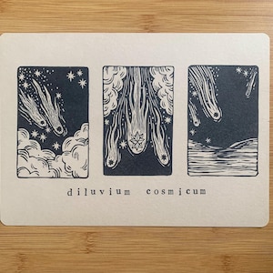 Può includere: Una stampa rettangolare con tre pannelli blu scuro raffiguranti eventi celesti. I pannelli mostrano comete, stelle e nuvole. Il testo "diluvium cosmicum" è stampato in nero in basso. La stampa è su sfondo color crema.