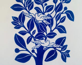 May include: A blue and white linocut print of a tree with two birds perched on its branches. The tree has large, stylized leaves and a thick trunk. The birds are depicted in a simple, elegant style, with their wings outstretched.