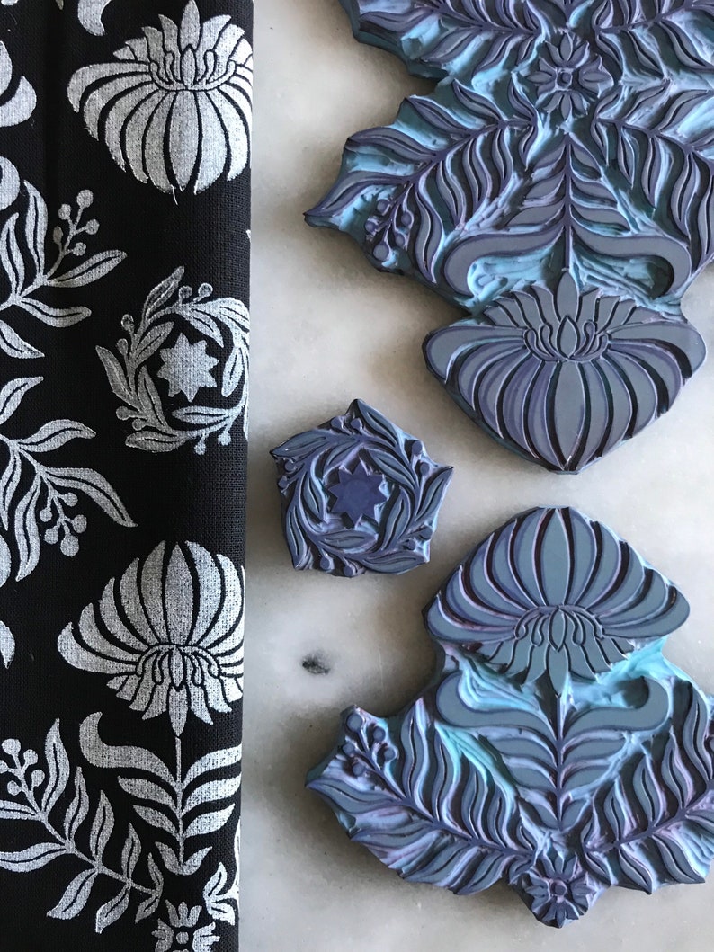 May include: Four blue and purple rubber stamps with floral and leaf designs. The stamps are on a white marble surface.