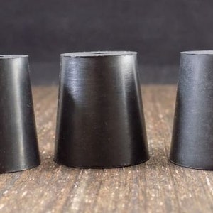 May include: Three black rubber bottle stoppers of different sizes. The stoppers are cone-shaped and have a small hole in the top.