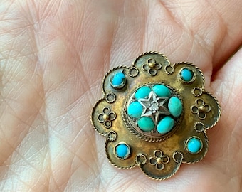 May include: Antique gold-tone brooch with a floral design. The brooch features turquoise-colored stones and a central star-shaped design with a small diamond. The brooch has a detailed, ornate design.