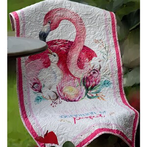 May include: A white quilted throw blanket with a pink flamingo and a baby flamingo design. The blanket has a pink border and the text "Definition of Perfect" is printed on the bottom.