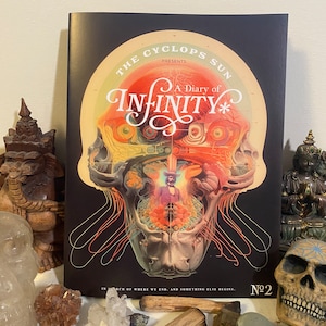 May include: A black and white comic book cover with a skull illustration. The skull is filled with colorful details, including eyes, teeth, and a brain. The title of the comic is "The Cyclops Sun Presents A Diary of Infinity" and the issue number is "No. 2".