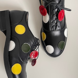 May include: A pair of black leather oxfords with colorful polka dots. The shoes have white, yellow, red, and green polka dots.