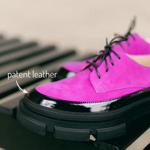 A pair of black and pink leather shoes with black laces and a platform black sole.