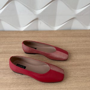 May include: A pair of red flats with a gold stripe detail. The shoes have a square toe and the brand name "MIAS" is visible on the left shoe.