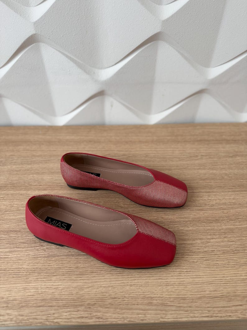 May include: A pair of red flats with a gold stripe detail. The shoes have a square toe and the brand name "MIAS" is visible on the left shoe.