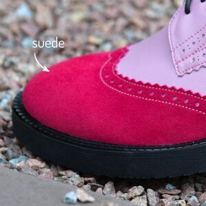 Pu&ograve; includere: Primo piano di una scarpa da donna rosa e rossa con punta in camoscio e suola nera. La parola "suede" &egrave; scritta sull'immagine.