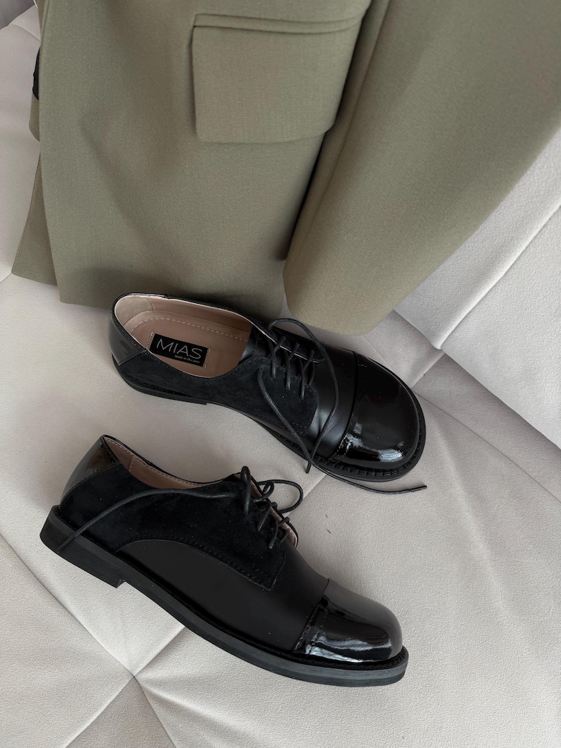 Op de afbeelding: Een paar zwarte leren veterschoenen met een laklederen neus. De schoenen hebben een ronde neus en een lage hak. De merknaam "MIAS" is zichtbaar aan de zijkant van een schoen.