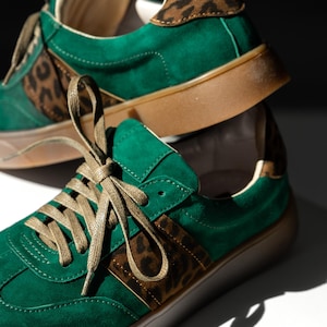 Green suede sneakers with brown leopard print accents. The sneakers have green laces and a brown sole.