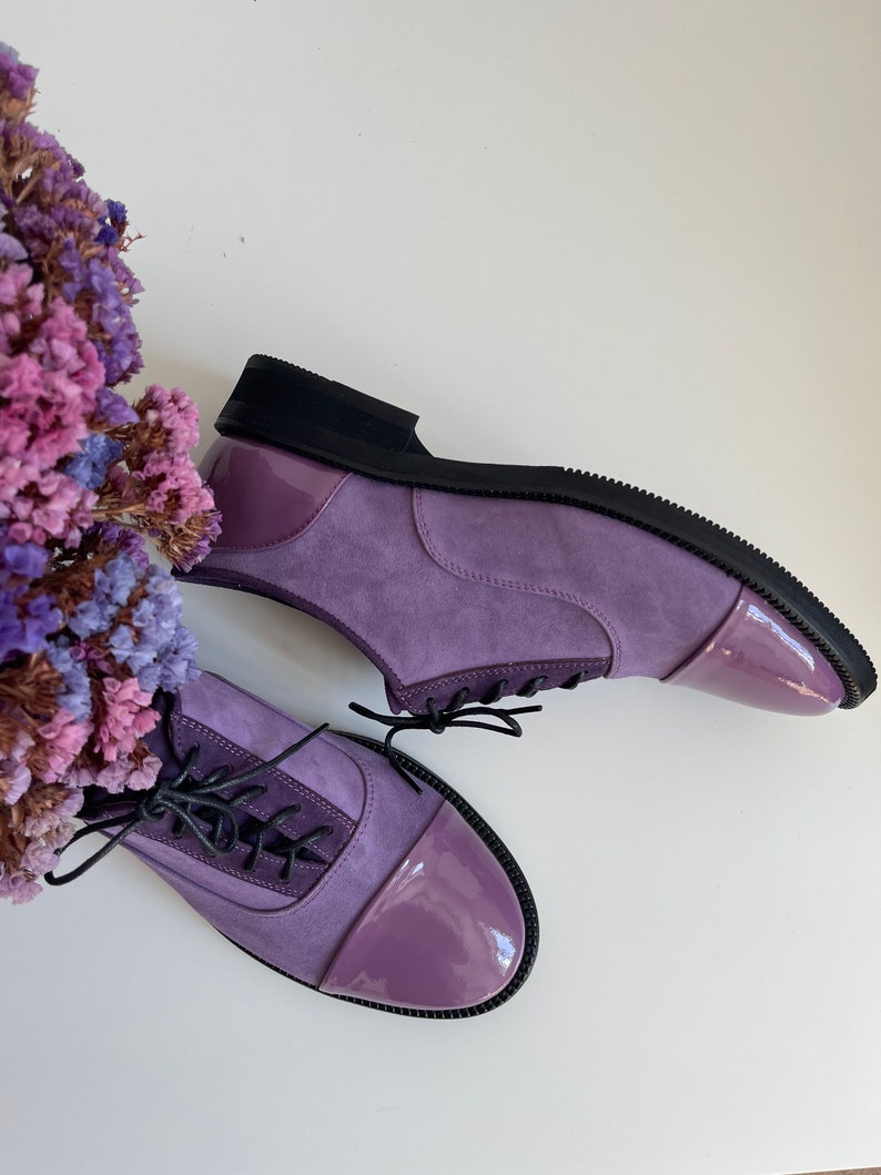 May include: A pair of purple suede lace-up shoes with a patent leather toe cap. The shoes have black laces and a black rubber sole.