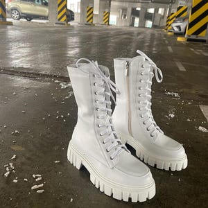 May include: A pair of white leather lace-up boots with chunky white soles. The boots have a zipper on the side and are made of smooth leather.