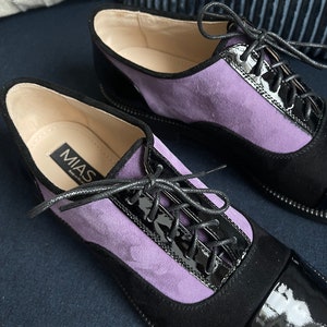 May include: A pair of black and purple suede and patent leather lace-up shoes with the brand name "MIAS" on the side.