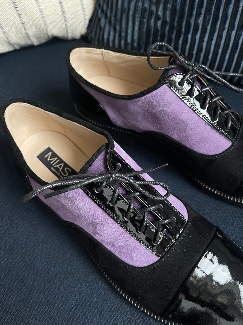 May include: A pair of black and purple suede and patent leather lace-up shoes with the brand name "MIAS" on the side.