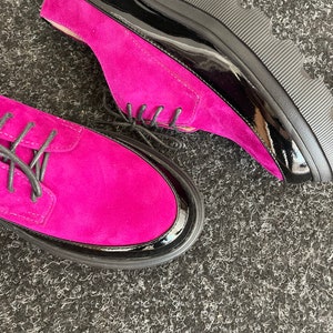 May include: A pair of fuchsia suede shoes with black patent leather trim and a chunky black platform sole.