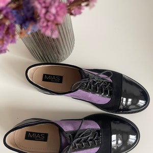 May include: A pair of purple and black leather lace-up shoes with a black patent leather toe. The shoes have the brand name "MIAS" printed on the inside.