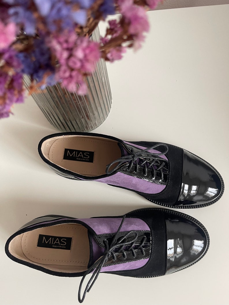 May include: A pair of purple and black leather lace-up shoes with a black patent leather toe. The shoes have the brand name "MIAS" printed on the inside.