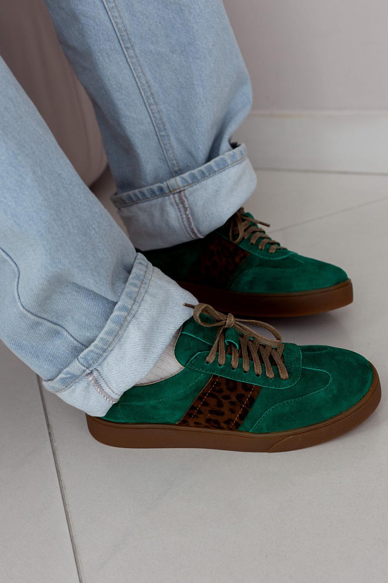 May include: A pair of green suede sneakers with brown leopard print accents and brown laces. The sneakers have a white sole.