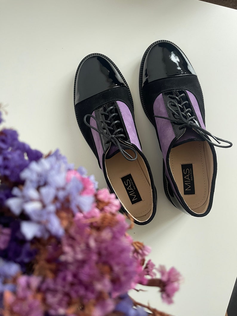 May include: A pair of black and purple lace-up shoes with a patent leather toe. The shoes have the brand name "MIAS" printed on the inside.