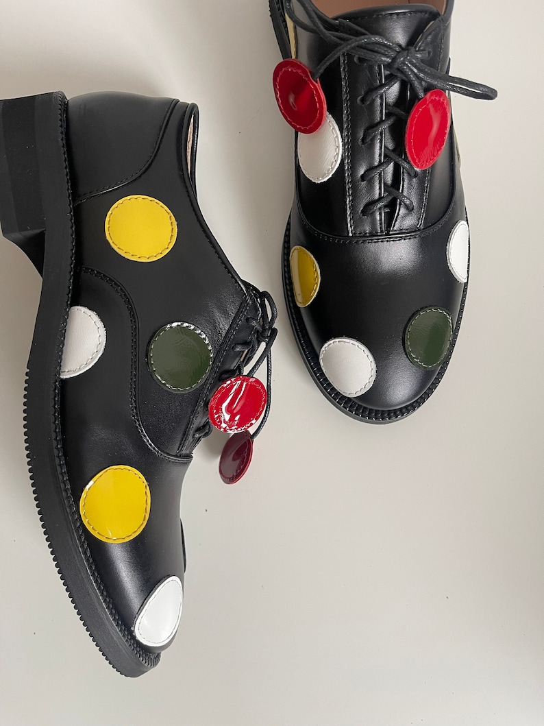 May include: A pair of black leather oxfords with colorful polka dots. The shoes have white, yellow, red, and green polka dots.