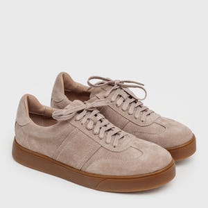 May include: A pair of light brown suede sneakers with a cream-colored sole. The sneakers have a lace-up closure and a classic design.