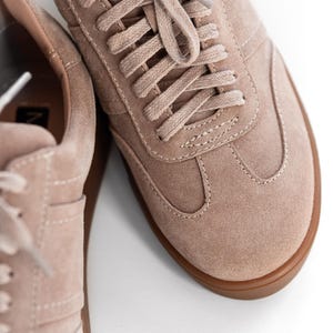 May include: A pair of light brown suede sneakers with a gum sole. The laces are tied in a criss-cross pattern.