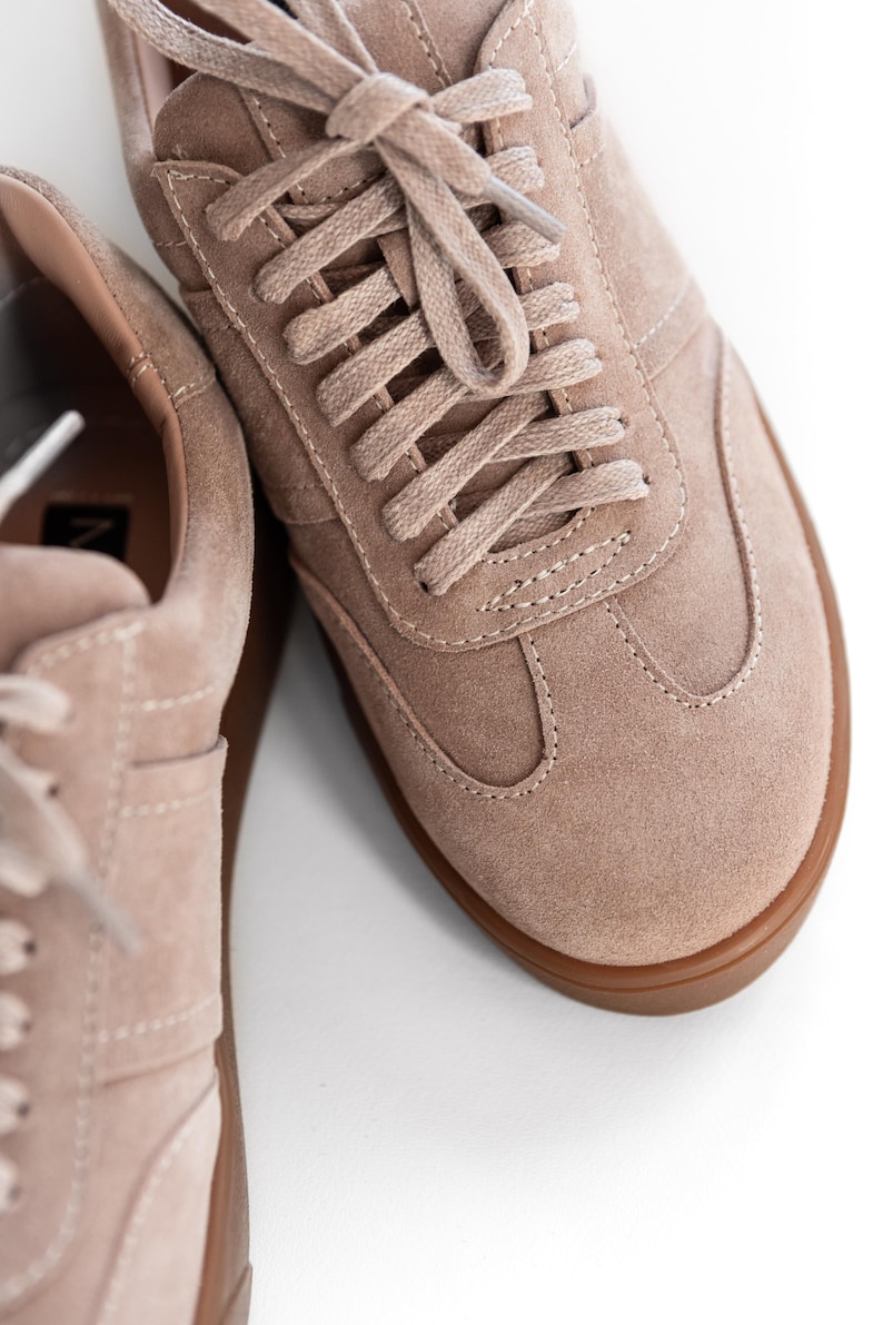 May include: A pair of light brown suede sneakers with a gum sole. The laces are tied in a criss-cross pattern.