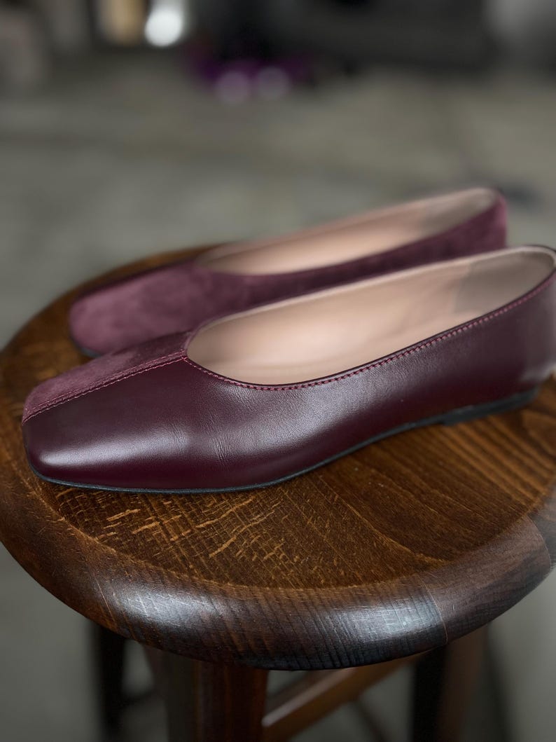 May include: A pair of burgundy leather flats with a square toe. The shoes have a suede toe cap and a leather upper.