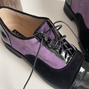 May include: Purple and black leather oxford shoes with lace-up closure. The shoes have a black patent leather toe cap and a black suede heel.