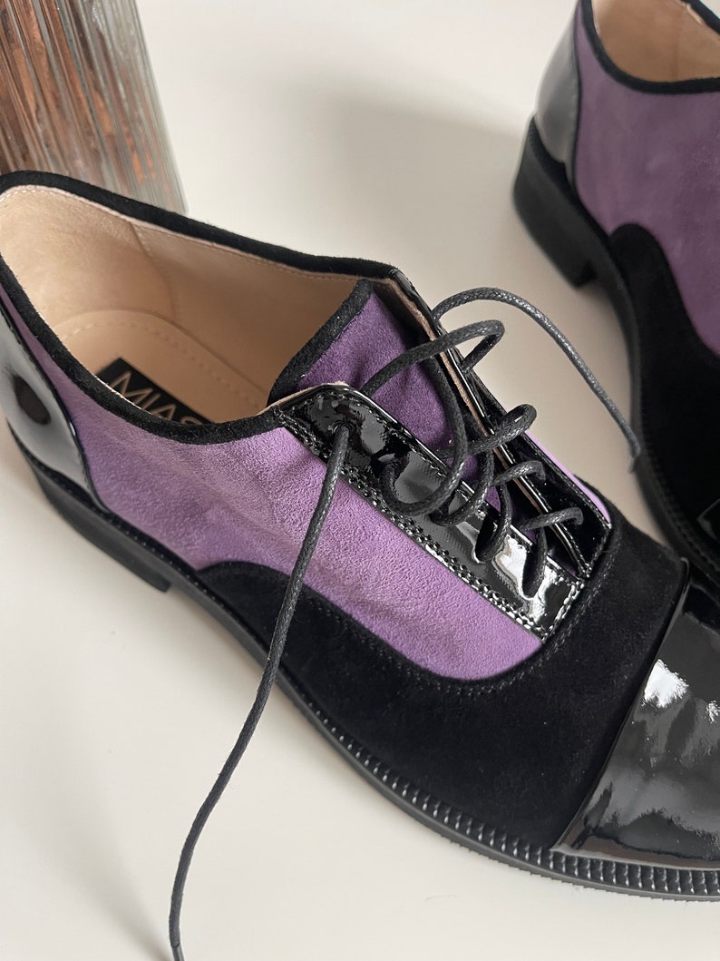 May include: Purple and black leather oxford shoes with lace-up closure. The shoes have a black patent leather toe cap and a black suede heel.