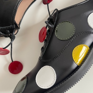 May include: Black leather lace-up shoes with colorful polka dots. The dots are yellow, green, white, and red.