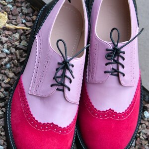 Pu&ograve; includere: Un paio di scarpe in pelle rosa e rosse con lacci neri e suola in gomma nera. Le scarpe hanno un bordo a festoni e una fodera in pelle.