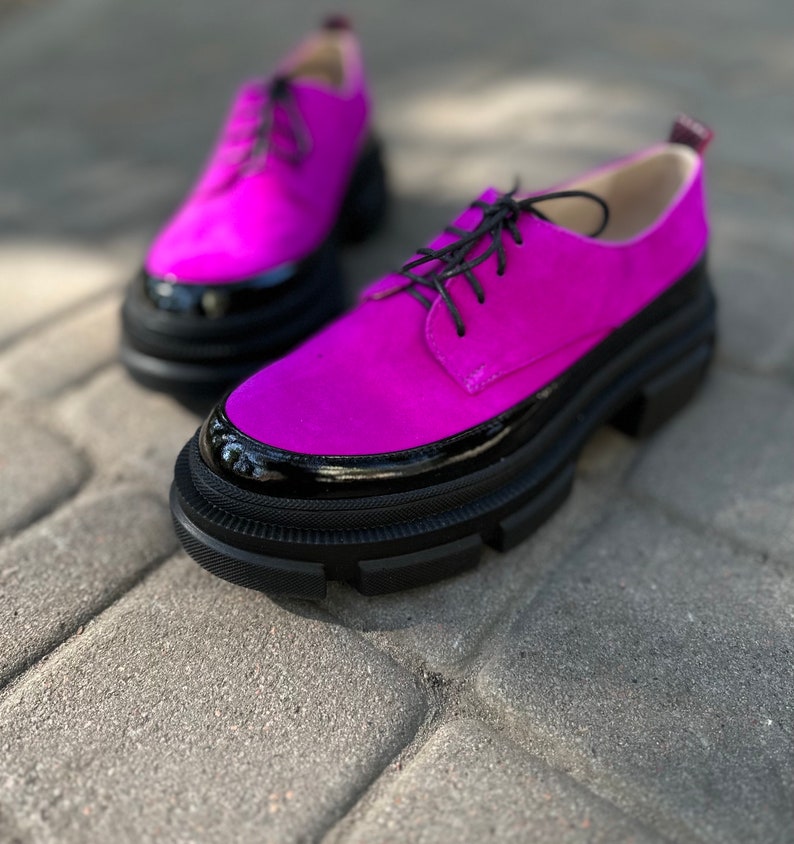 A pair of bright pink suede lace-up shoes with black patent leather trim and chunky black soles